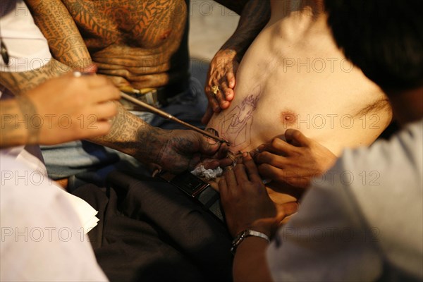 THAILAND, Phuket, Man having tattoo applied to torso.