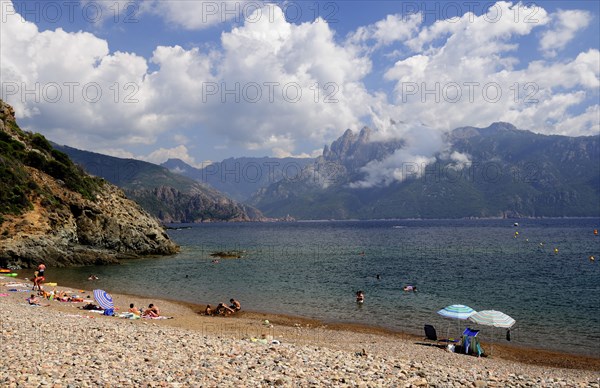 FRANCE, Corsica, Golfe Di Porto, "Plage De Bussaglia, shingle beach with umbrellas & bathers & Capo d'Orta mountains"