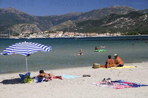 FRANCE, Corsica, St Florent, Bathers & sandy beach with St Florent old town in distance