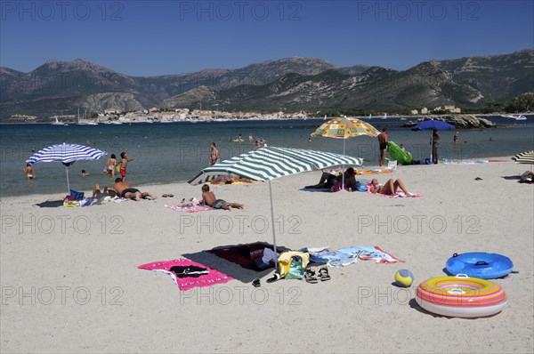 FRANCE, Corsica, St Florent, Bathers & sandy beach with St Florent old town in distance