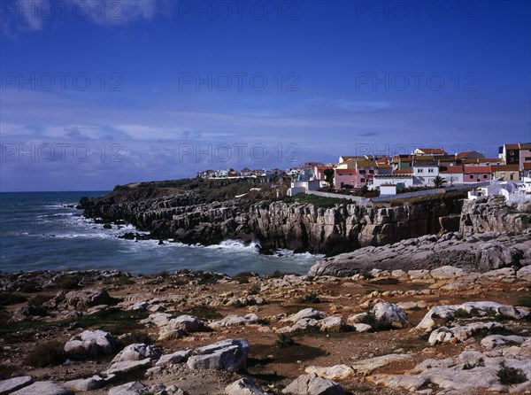 PORTUGAL, Estremadura, Ribatejo, Peniche. Atlantic Ocean town. View across low cliffs and rocky foreshore towards the south side of  town with colourful painted houses
