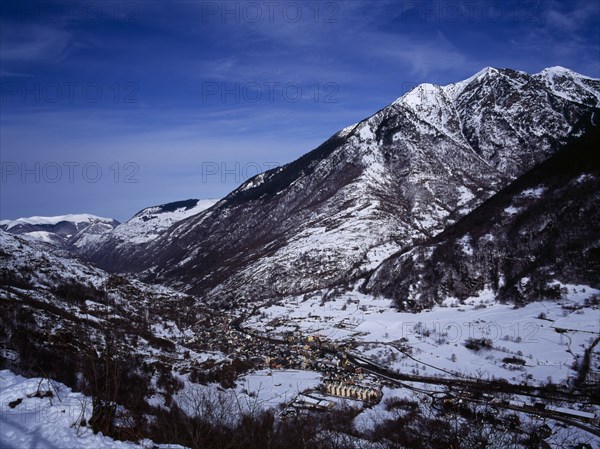 SPAIN, Catalonia, Lleida, Pyrenees. Elevated view north east from the route to Col du Portillon over snow covered valley looking over the rooftops of the town of Ville Bossost. The mountain Montlude 2518 metres 8246 feet and the river Valle Garona.