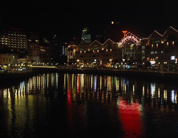 SINGAPORE, Cityscapes, Clarke Quay on the Singapore River. Waterside shops and restaurants illuminated at night with multi coloured lights reflected on the water