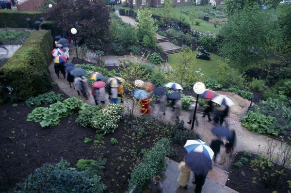 ENGLAND, East Sussex, Glyndebourne, Opera attendees walking through the gardens holding umbrellas in the rain.