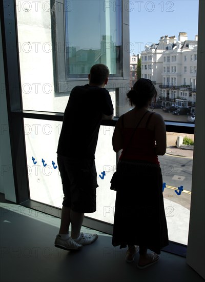 ENGLAND, East Sussex, Eastbourne, Young silhouetted couple looking out the window of the Towner Gallery building toward the seafront.