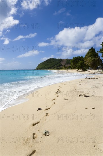 WEST INDIES, St Vincent & The Grenadines, Canouan, South Glossy Beach in Glossy bay with footprints in the sand and waves from the turqoise sea breaking on the shore.