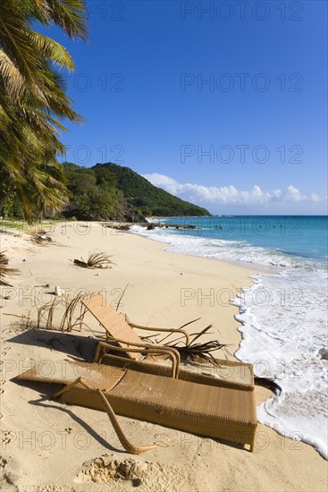 WEST INDIES, St Vincent & The Grenadines, Canouan, South Glossy Beach in Glossy bay with two damaged wooden sunbeds in the sand and waves from the turqoise sea breaking on the shore.