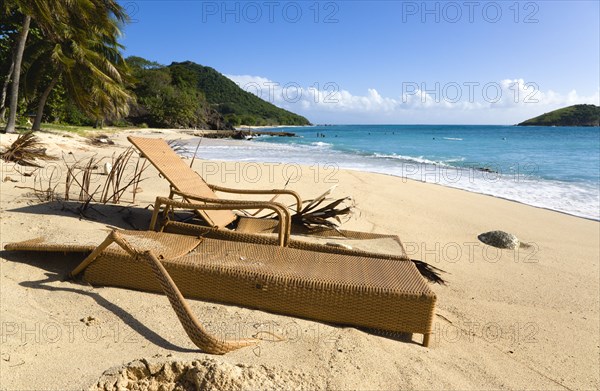 WEST INDIES, St Vincent & The Grenadines, Canouan, South Glossy Beach in Glossy bay with two damaged wooden sunbeds in the sand and waves from the turqoise sea breaking on the shore.