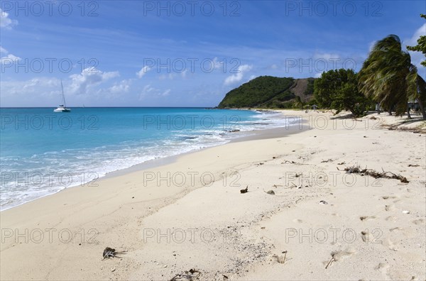 WEST INDIES, St Vincent & The Grenadines, Canouan, South Glossy Beach in Glossy bay with waves from the turqoise sea breaking on the shore and a yacht at anchor in the bay.