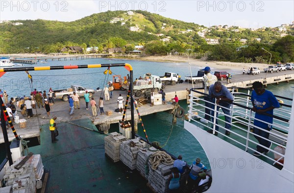 WEST INDIES, St Vincent & The Grenadines, Canouan, Charlestown Bay Inter island ferry at jetty with people walking amongst trucks with cargo unloaded from boat.