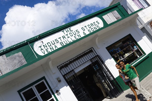 WEST INDIES, Grenada, Carriacou, Hillsborough Hardware shop The Industrious Stores owned by Vena Bullen and Sons with two smiling girls walking past in the main street.