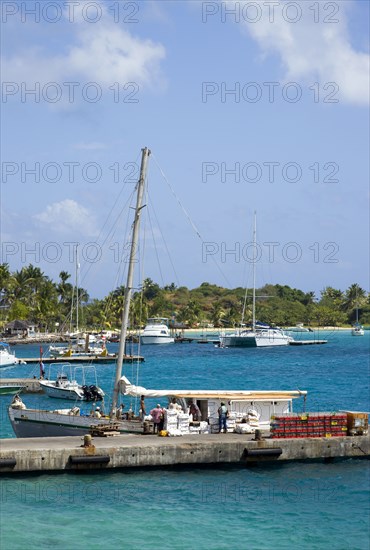 WEST INDIES, St Vincent & The Grenadines, Union Island, Inter island supply boat unloading provisions onto the main jetty in Clifton with yachts behind moored by the Anchorage Yacht Club in Clifton Harbour.