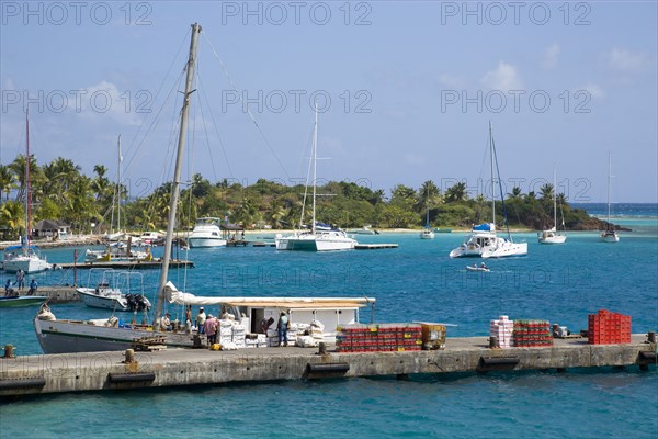 WEST INDIES, St Vincent & The Grenadines, Union Island, Inter island supply boat unloading provisions onto the main jetty in Clifton with yachts behind moored by the Anchorage Yacht Club in Clifton Harbour.