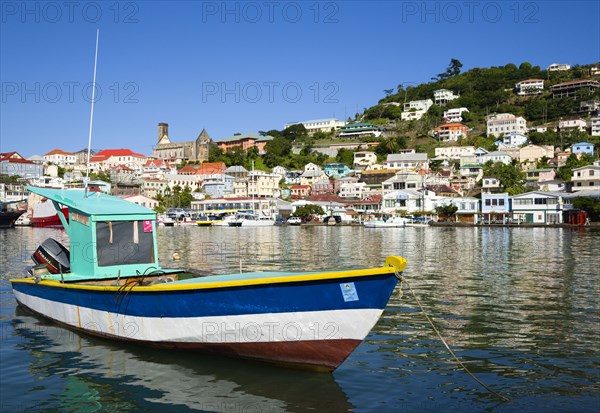 WEST INDIES, Grenada, St Georges, The Carenage in the capital with houses lining the hillside and a fishing boat moored in the harbour.