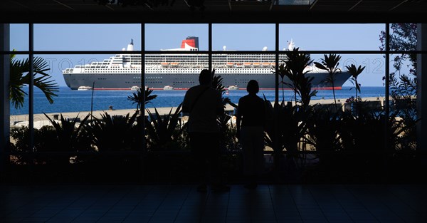 WEST INDIES, Grenada, St Georges, Tourists in the Cruise Ship Terminal looking out through the glass window towards the Queen Mary 2 liner moored offshore.