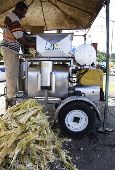 WEST INDIES, Grenada, St George, Man feeding sugar cane into a mobile cane juice machine beside Grand Anse beach.