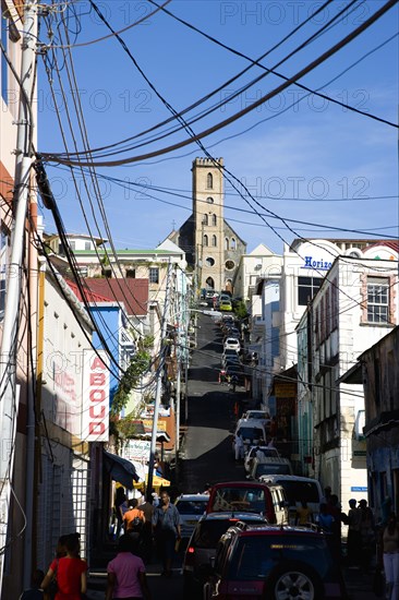 WEST INDIES, Grenada, St George, St Juille Street with overhead power cables busy with traffic and pedestrian shoppers leading to the hurricane damaged and roofless Roman Catholic Cathedral in the capital.