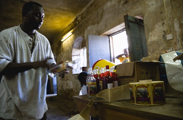 WEST INDIES, Grenada, St Patrick, Male worker hand labelling the bottles at the River Antoine rum distillery.