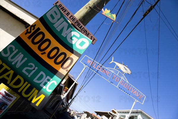 WEST INDIES, Grenada, St John, Town of Gouyave with a metal sign above the main road through the fishing town reading Welcome To Gouyave The Fishing Capital Of Grenada with a sign on a lamp post advertising the weekly bingo .