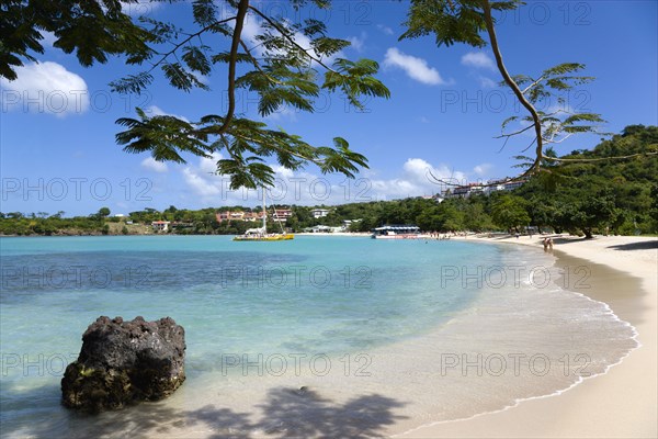 WEST INDIES, Grenada, St George, Gentle waves on BBC Beach in Morne Rouge Bay with tourists in the sea on the beach and aboard their tour catamaran in the aquamarine water.