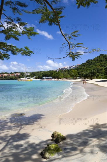 WEST INDIES, Grenada, St George, Gentle waves on BBC Beach in Morne Rouge Bay with tourists in the sea on the beach and aboard their tour catamaran in the aquamarine water.