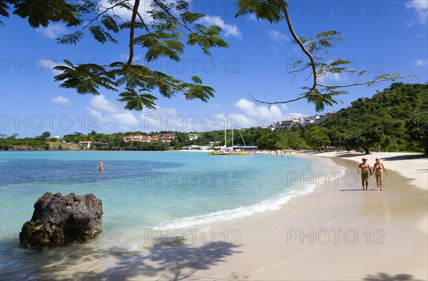 WEST INDIES, Grenada, St George, Gentle waves on BBC Beach in Morne Rouge Bay with tourists in the sea on the beach and aboard their tour catamaran in the aquamarine water.