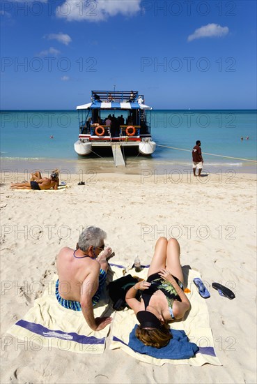 WEST INDIES, Grenada, St George, Tourists from cruise ships on BBC Beach in Morne Rouge Bay in the aquamarine sea and on the beach sunbathing beside their day trip catamaran the Rhum Runner.
