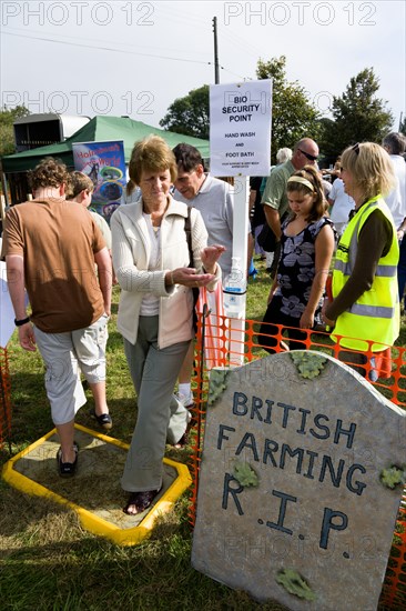 ENGLAND, West Sussex, Findon, Findon village Sheep Fair People passing through a Bio Security point for hand wash and foot bath to prevent spread of foot and mouth with a sign on a mock gravestone reading British Farming RIP.