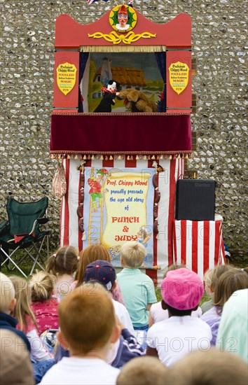 ENGLAND, West Sussex, Findon, Findon village Sheep Fair A group of children sitting on the ground watching a Punch and Judy glove puppet show.
