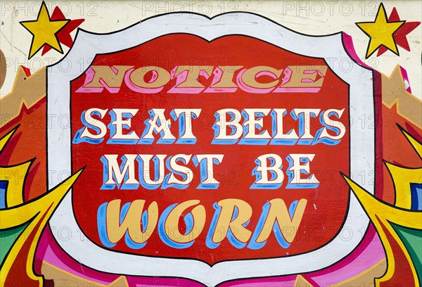 ENGLAND, West Sussex, Findon, Findon village Sheep Fair Colourful red sign on a fairground ride that reads Notice Seat Belts Must Be Worn.