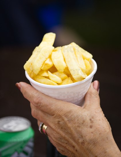 ENGLAND, West Sussex, Findon, Findon village Sheep Fair Elderly lady holding a polystyrene mug full of potato fries in one hand.