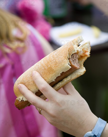 ENGLAND, West Sussex, Findon, Findon village Sheep Fair Teenage girl holding a hot dog with tomato ketchup and onions with a bite taken out of it.