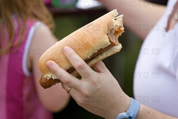 ENGLAND, West Sussex, Findon, Findon village Sheep Fair Teenage girl holding a hot dog with tomato ketchup and onions with a bite taken out of it.
