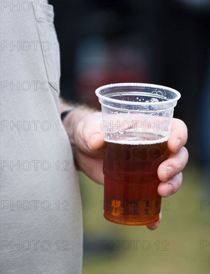 ENGLAND, West Sussex, Findon, Findon village Sheep Fair Man with a fat stomach holding a plastic pint measure mug containing bitter beer in his left hand.
