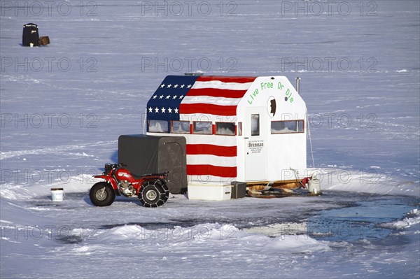 USA, New Hampshire, Harrisville, Ice fishermen on Silver Lake. cabin painted with US flag and Live Free or Die message.