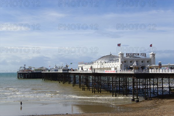 ENGLAND, East Sussex, Brighton, The Pier at low tide with a woman walking towards the water.