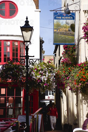 ENGLAND, East Sussex, Brighton, The Lanes Old fashioned streetlight lamppost outside The Sussex Pub with flowers in window boxes and hanging baskets and people walking in the narrow alley.