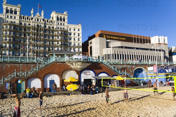 ENGLAND, East Sussex, Brighton, Young people playing beach volleyball on sand on the seafront with the De Vere Grand Hotel and The Brighton Centre beyond.