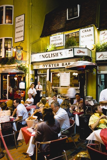 ENGLAND, East Sussex, Brighton, The Lanes Englishs Oyster Bar and Seafood Restaurant exterior at night with people sitting outside at tables eating a meal under a patio heater.