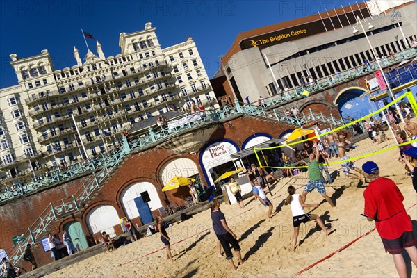 ENGLAND, East Sussex, Brighton, Young people playing beach volleyball on sand on the seafront with the De Vere Grand Hotel and The Brighton Centre beyond.