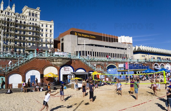 ENGLAND, East Sussex, Brighton, Young people playing beach volleyball on sand on the seafront with the De Vere Grand Hotel and The Brighton Centre beyond.