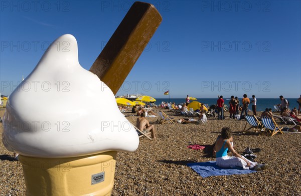ENGLAND, East Sussex, Brighton, People sunbathing on the pebble shingle beach with a giant fibreglass model of an ice cream cone in the foreground.