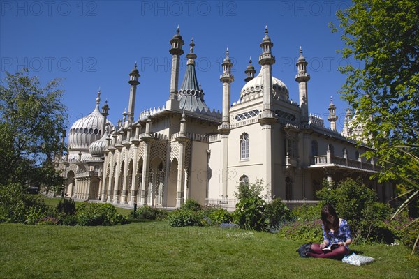 England, East Sussex, Brighton, The Royal Pavilion, 19th century retreat for the then Prince Regent, Designed by John Nash in a Indo Sarascenic style, with girl reading in the foreground.