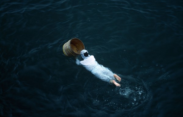 Japan, Honshu, Toba, Traditional female pearl diver swimming in the water with wooden barrel for collecting oysters at the Mikimoto Pearl Farm in Mie Prefecture in Kansai Region.
