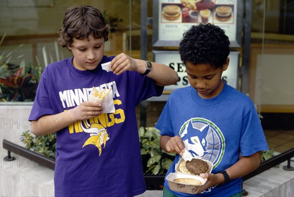 England, East Sussex, Brighton, Multicultural group of young boys adding salt to their takeaway fast food meal of hamburger and french fries or chips.