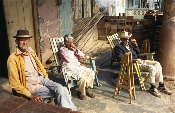 CUBA, Vinales, Elderly woman and two men sitting outside building.