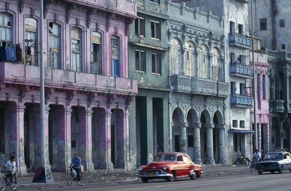 CUBA, Havana, Malecon street scene with crumbling exterior facades of buildings painted pink, blue and green.  Passing cyclists and old cars.