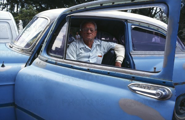 CUBA, Havana, Old Havana, Man in blue car framed by open window.