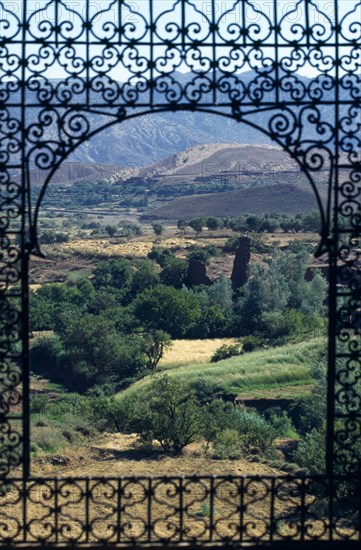 MOROCCO, High Atlas Mountains, Telouet, The Dar glaoui kasbah. View through an arched window with decorative metalwork surround to distant mountains.