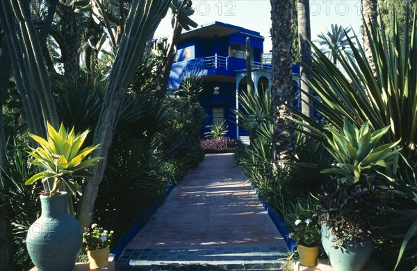 MOROCCO, Marrakesh, Jardin Marjorelle known as the residence of Yves Saint-Laurent, view along plant lined path to the house.